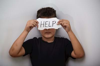 boy covering face with sign saying help